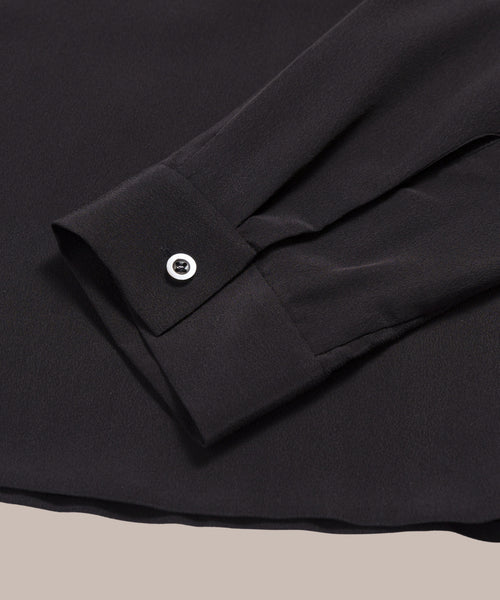 A close-up of the cuff and sleeve of the Silk Sloane Shirt, a black button-down with a single white button, laid flat on a neutral surface.
