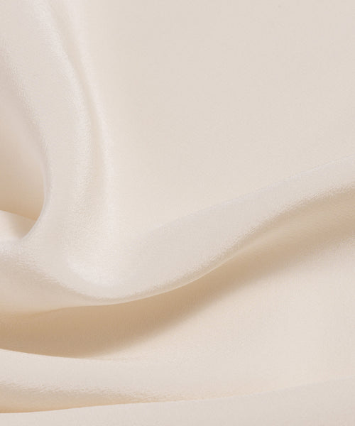 Close-up of the Silk Sloane Shirt showcases smooth, sandwashed silk in a cream shade, featuring gentle folds and a soft, lustrous texture.