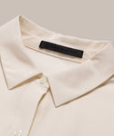 Close-up of the Silk Sloane Shirt in ivory silk with white buttons and a black jenni kayne label inside the collar, displayed on a beige background. This sandwashed silk shirt offers a refined, elegant touch.