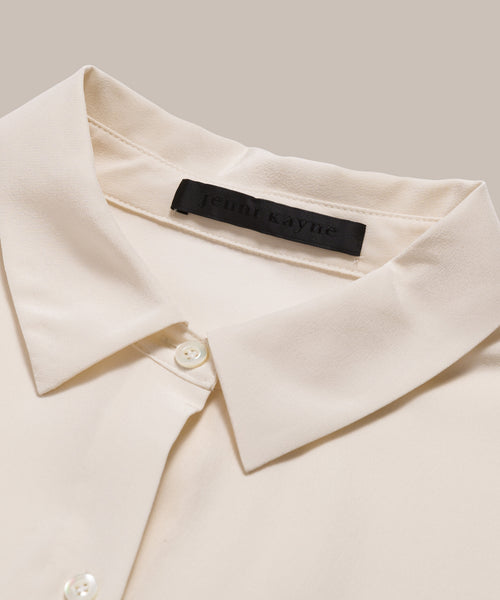 Close-up of the Silk Sloane Shirt in ivory silk with white buttons and a black jenni kayne label inside the collar, displayed on a beige background. This sandwashed silk shirt offers a refined, elegant touch.