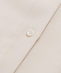 Close-up of the Silk Sloane Shirts sandwashed silk fabric, featuring a shiny white button sewn on. The material looks smooth and soft, with detailed stitching around the button.