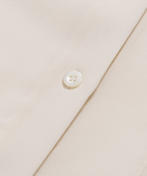 Close-up of the Silk Sloane Shirts sandwashed silk fabric, featuring a shiny white button sewn on. The material looks smooth and soft, with detailed stitching around the button.