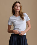 Woman wearing a baby blue t-shirt and navy pants against a brown background.