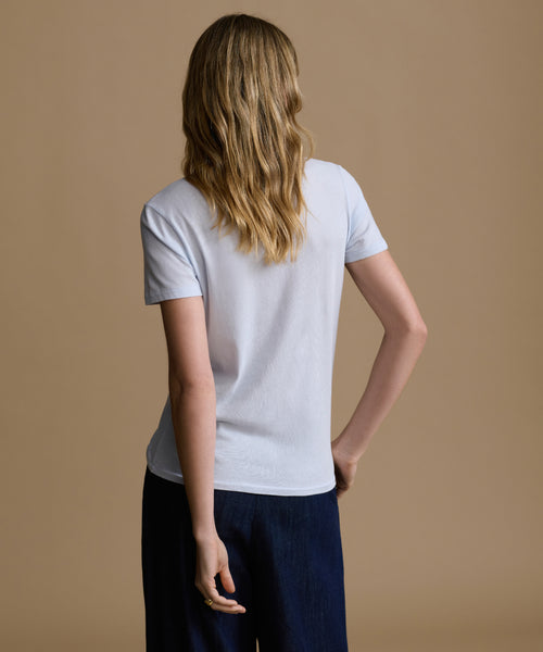 Woman wearing a baby blue t-shirt and navy pants against a brown background.