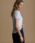 Woman wearing a baby blue t-shirt and navy pants against a brown background.
