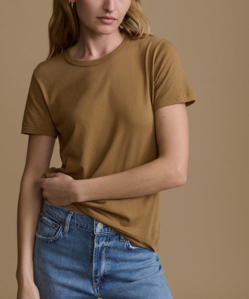 Woman wearing a brown top and blue jeans against a beige background