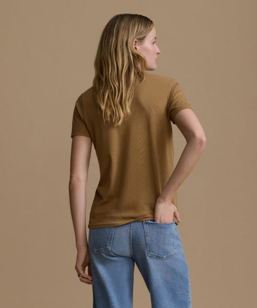 Woman wearing a brown top and blue jeans against a beige background