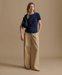 Woman wearing a navy blue t-shirt and beige pants on a brown background