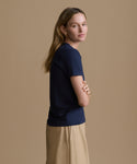 Woman wearing a navy blue t-shirt and beige pants against a brown background