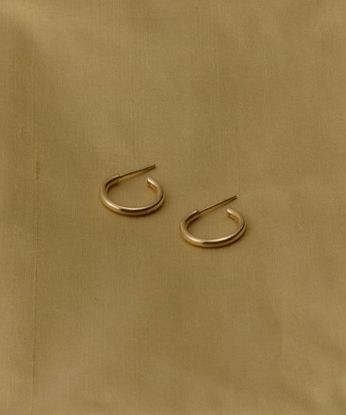 The Small Eloise Hoops from Jenni Kayne, crafted in 14k gold, rest parallel with a slight gap on a light brown fabric backdrop, embodying the timeless elegance of heirloom jewelry.