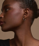 A close-up side profile of a woman with dark skin wearing the Small Eloise Hoops. Her hair is pulled back as she looks to the left against a plain beige background.