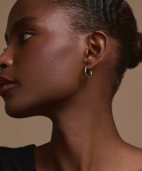 A close-up side profile of a woman with dark skin wearing the Small Eloise Hoops. Her hair is pulled back as she looks to the left against a plain beige background.