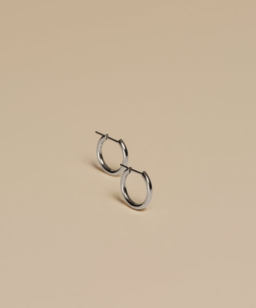 A pair of Small Eloise Hoops are shown on a beige surface under soft lighting, with subtle shadows highlighting their design.