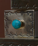 A close-up of the Small Stamped Matchbox with Turquoise shows its ornate silver design, detailed engravings, and a striking turquoise stone with dark veining set in the center of the lid.