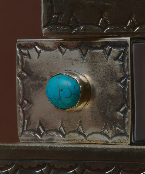 A close-up of the Small Stamped Matchbox with Turquoise shows its ornate silver design, detailed engravings, and a striking turquoise stone with dark veining set in the center of the lid.