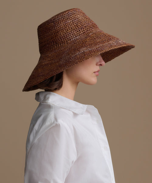 Woman wearing a chocolate soleil hat against a beige background
