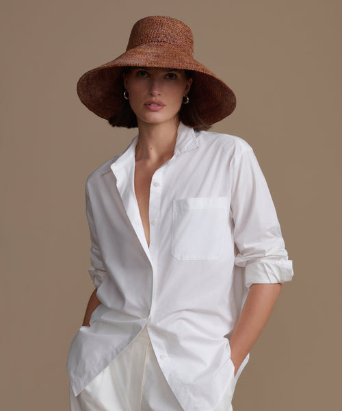 Woman wearing a white shirt and chocolate soleil hat against a beige background