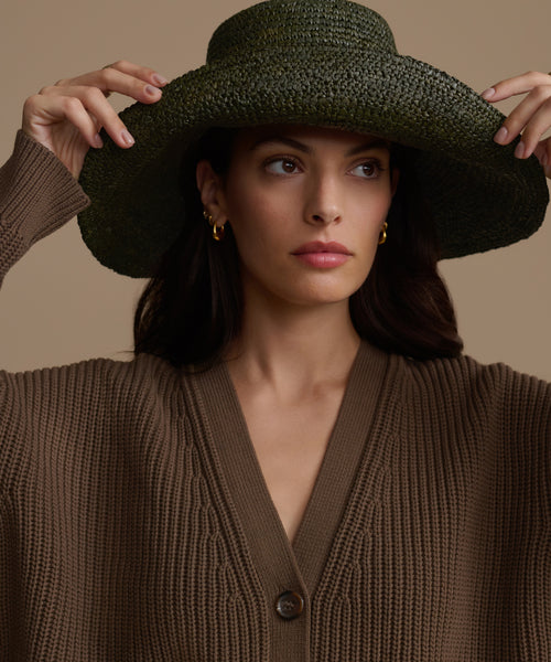 Woman wearing a Olive Soleil hat and brown cardigan against a beige background