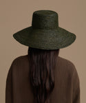 Person wearing a Olive Soleil hat and brown sweater on a beige background