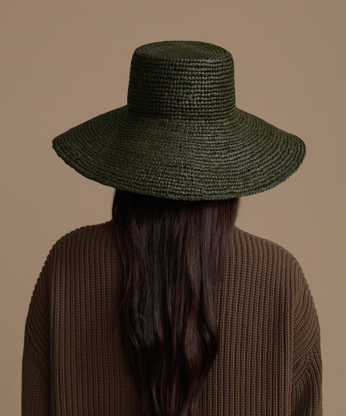 Person wearing a Olive Soleil hat and brown sweater on a beige background