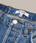 Close-up view of the waistband and button of The Standard blue denim straight leg jeans. The brand label reads RE/DONE, size tag 25. Inspired by Men’s 501 Levi’s, they feature gold stitching and an “Original” metal button.
