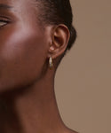 Close-up of a woman's ear wearing Stevie Grey Diamond Hoops—14k gold with textured design. Her skin is smooth and hair pulled back against a neutral beige background, highlighting these timeless heirloom earrings for any occasion.