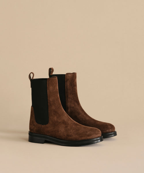 The Suede Alden Boot features brown suede, black elastic side panels, and weather-friendly rubber soles, shown against a plain beige background.