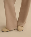 A close-up of a person wearing wide-legged tan pants and the Suede Ashby Clog with a shearling-lined footbed, standing on a light beige background.