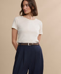 A person wears a short-sleeve cream t-shirt tucked into high-waisted navy trousers with the Suede Danner Belt, standing against a beige background and looking to the side.