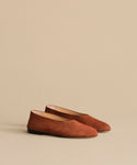 The Suede Elodie Flat features a simple, minimalist design and feminine silhouette in brown suede, shown against a plain beige background.