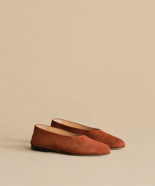 The Suede Elodie Flat features a simple, minimalist design and feminine silhouette in brown suede, shown against a plain beige background.