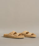 The Suede Hutton Slide Sandal, with tan suede, two adjustable buckle straps, and textured rubber soles, is shown on a gray background—an effortless and stylish option for warm weather.