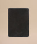 The Suede Passport Holder in black features subtle edge stitching and is displayed on a light beige background—an elegant touch for your travel essentials.
