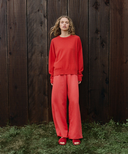Woman wearing a red outfit standing against a wooden fence.