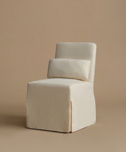 An upholstered accent chair in a warm cream fabric, featuring a tall backrest and a matching rectangular lumbar pillow, set against a solid beige background.