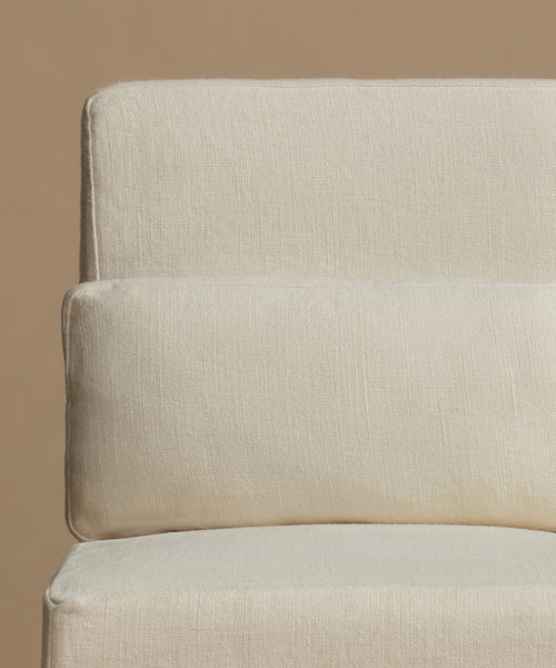Close-up of a cream-colored textured fabric cushion on a matching upholstered furniture piece against a warm beige background.