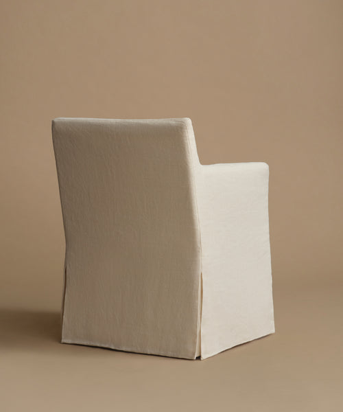 A single upholstered chair shown from the back in a studio setting, covered in a light warm off-white fabric against a beige background.