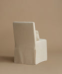 An upholstered armchair covered in a textured cream linen slipcover, shown from a three-quarters angle against a solid beige studio background.