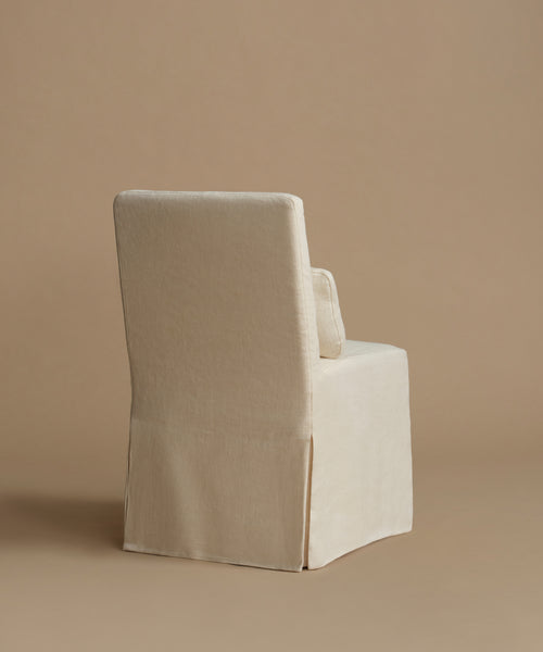 An upholstered armchair covered in a textured cream linen slipcover, shown from a three-quarters angle against a solid beige studio background.
