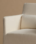Close-up of a cream-colored upholstered armchair with a textured linen-like fabric, featuring a square armrest and a matching back cushion against a solid warm beige background.