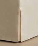 Close-up of a beige upholstered furniture corner with a skirted edge and visible fabric texture.