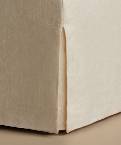 Close-up of a beige upholstered furniture corner with a skirted edge and visible fabric texture.