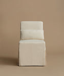 An upholstered accent chair with a tiered backrest and a skirted base, covered in a textured cream fabric, set against a solid warm beige background.