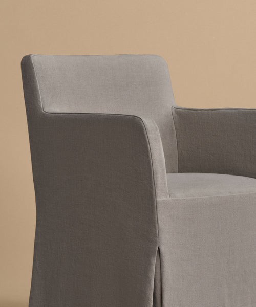 The Sunset Dining Arm Chair features a slipcover in soft gray fabric and clean, straight lines, displayed against a plain beige background.