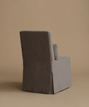A single upholstered armchair shown from the back in a studio setting, with a tall back, slim arms, and a skirted base. The chair is covered in a textured fabric in a warm gray-brown tone against a solid beige backdrop.