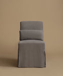 A gray upholstered chair with a high back, two loose back cushions, and a skirted base, photographed against a solid warm beige studio background.