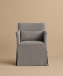 The Sunset Dining Arm Chair is a modern gray chair with a slipcover, matching rectangular cushion, skirted base, and straight armrests, displayed against a plain beige background.