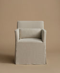 A slipcovered armchair with a matching back cushion, upholstered in a light beige textured fabric, set against a solid warm beige background.