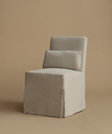 A light beige upholstered armless chair with a matching rectangular back cushion, shown on a warm beige studio background.