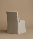 A single upholstered armchair shown from the back, covered in a light warm gray or greige fabric, set against a solid warm beige studio background.